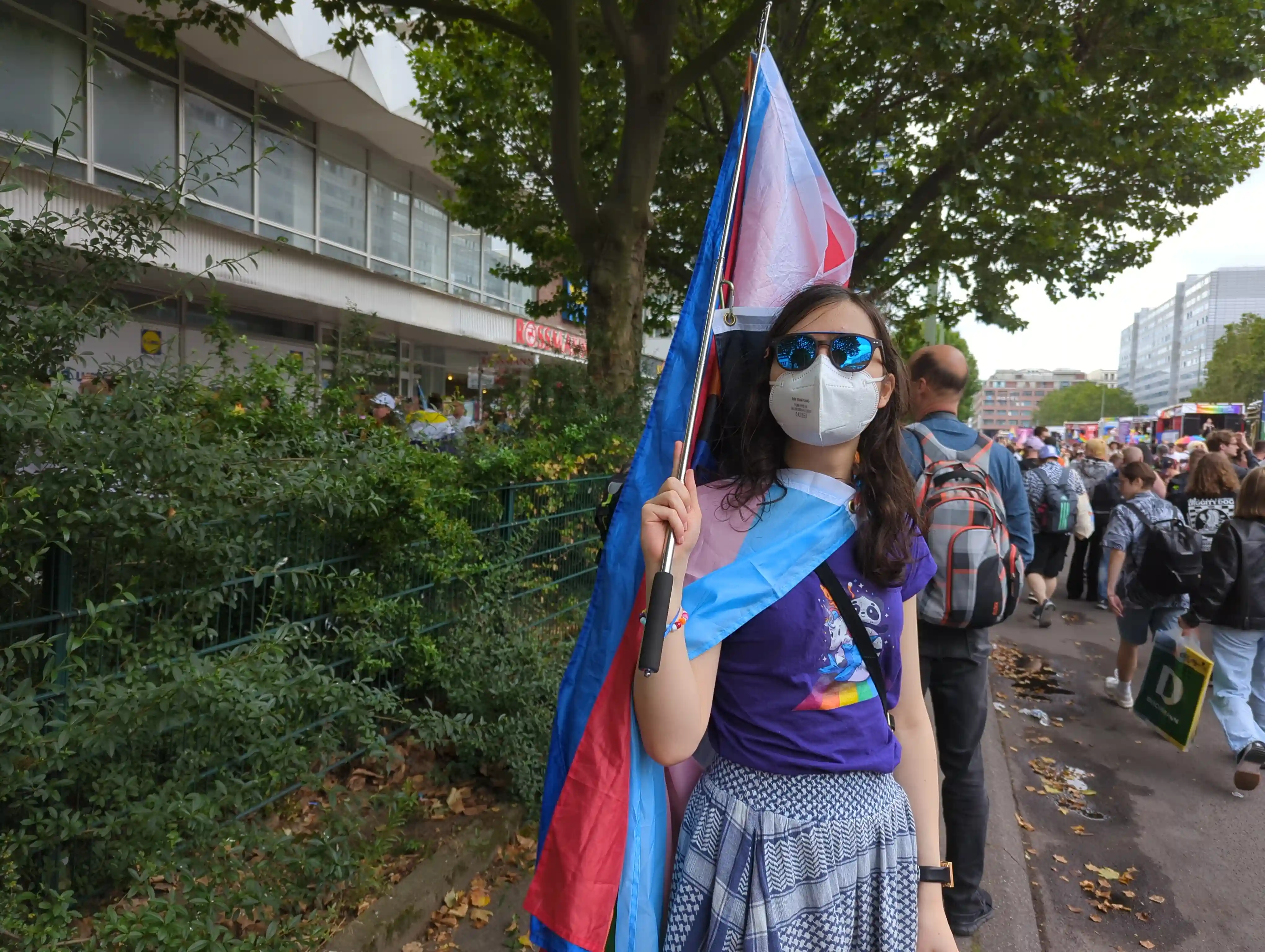 Artemis at CSD, holding a pride flag and wearing one as a cape